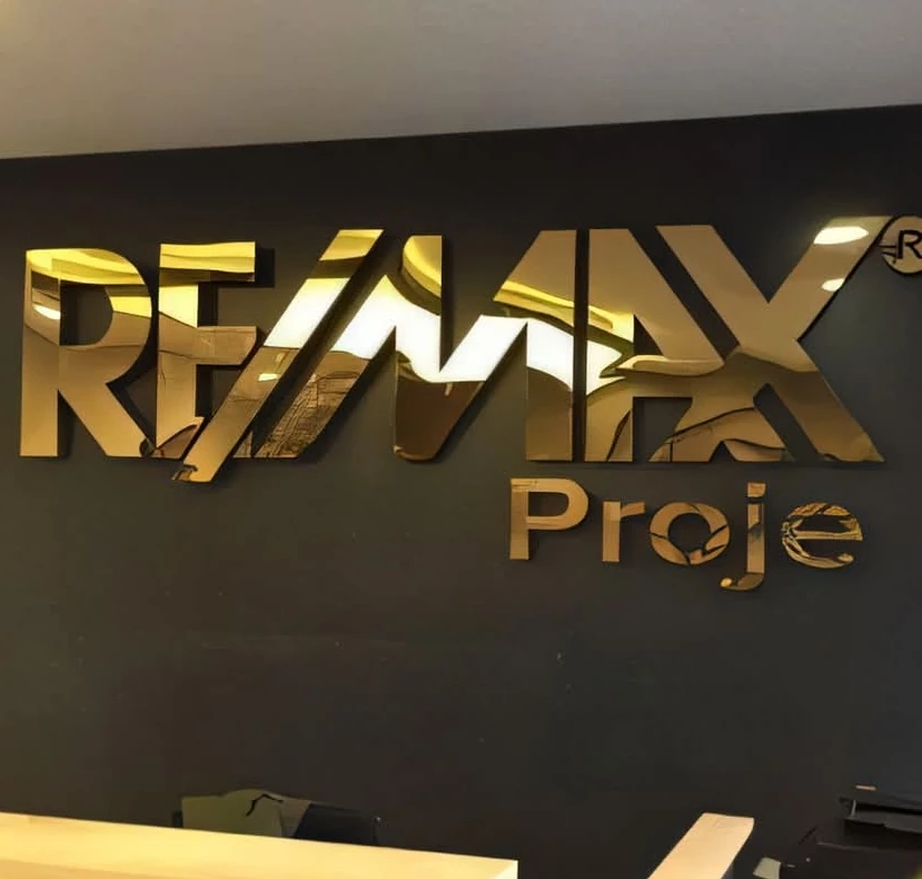 حروف استانلس ذهبي عاكسة لشعار RE/MAX على جدار داكن